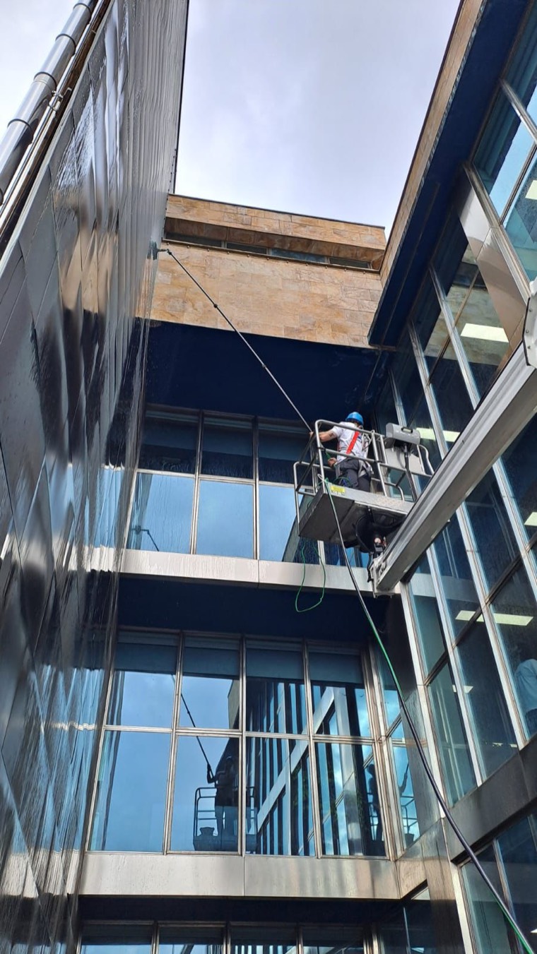 Operario de Limpatex limpiando con pértiga la fachada acristalada de un edificio desde una plataforma elevadora